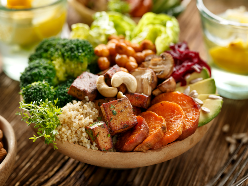 A vibrant Nourish Bowl featuring quinoa, cherry tomatoes, cucumbers, spinach, roasted sweet potatoes, sesame seeds, and tahini dressing, garnished with fresh herbs on a rustic wooden table.