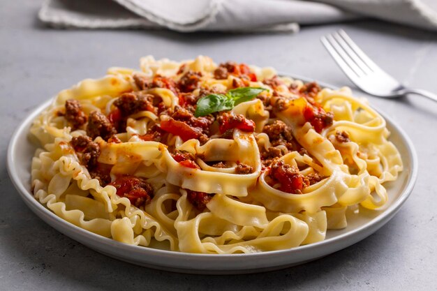 A close-up view of Mafaldine pasta served in a white bowl, garnished with fresh herbs and a rich Bolognese sauce.